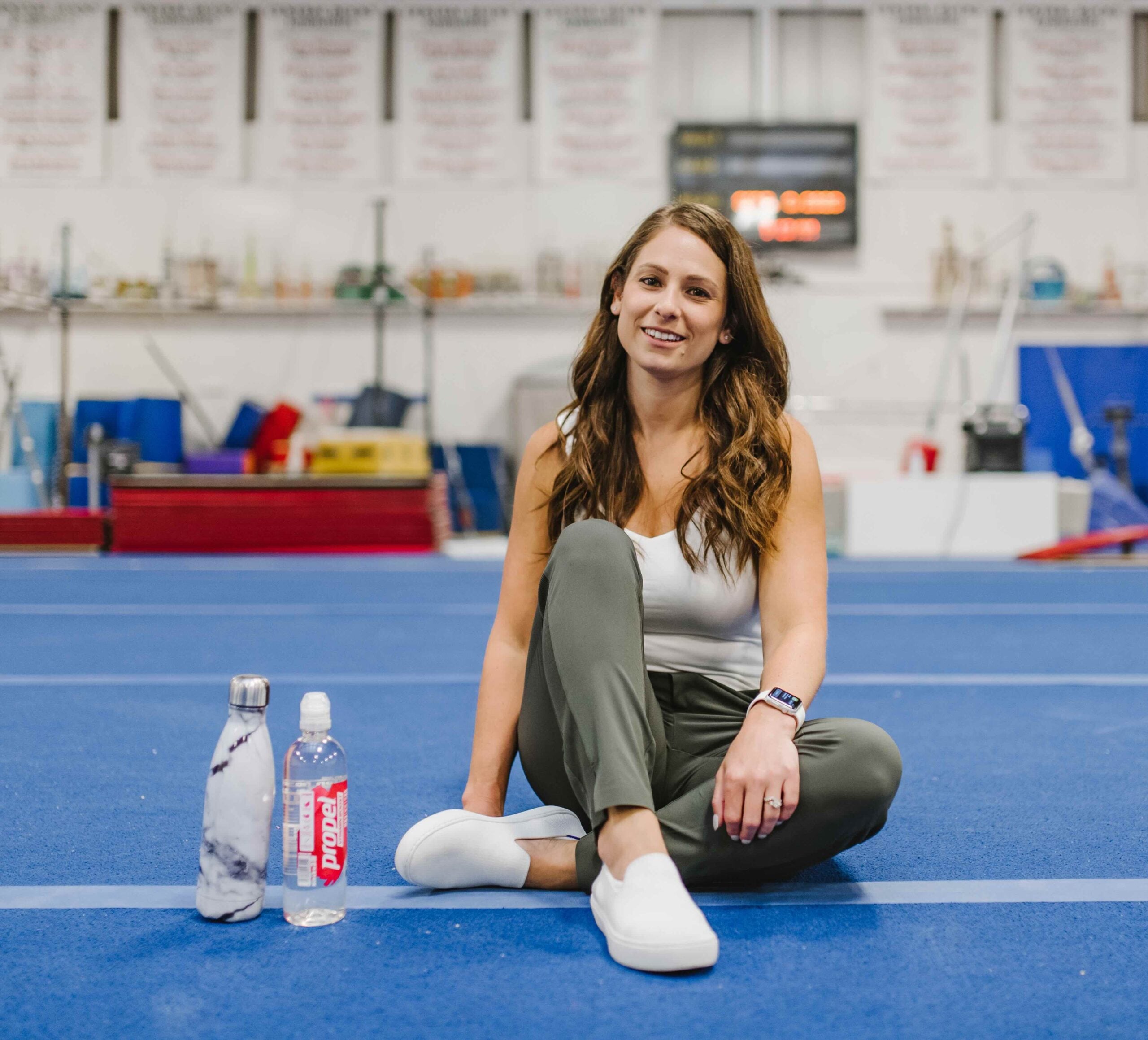 Kerry, Board-Certified Sports Dietitian for Gymnasts, sitting cross-legged and smiling with a water bottle beside her