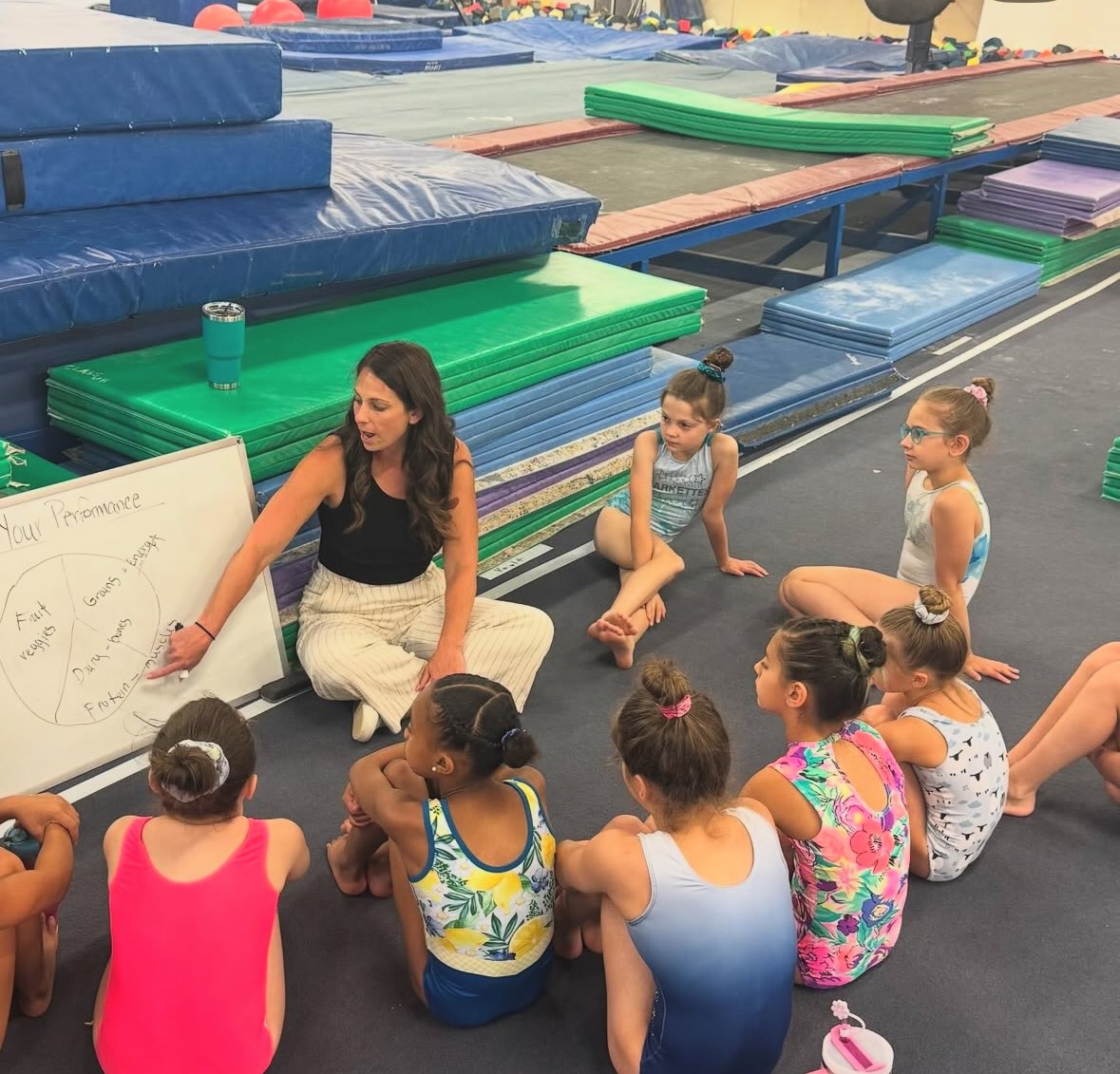 Kerry kneeling and talking with a small group of young gymnasts during a workshop or team session
