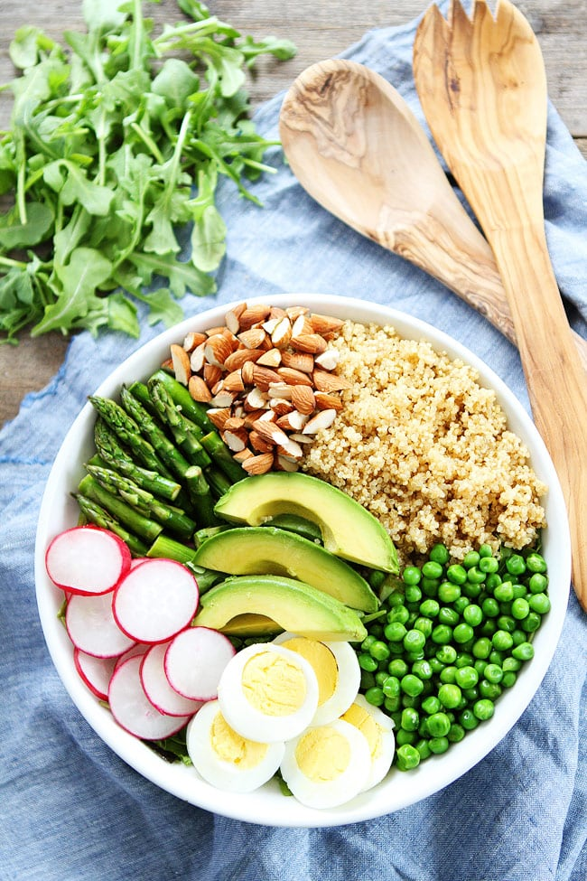 a colorful mixed power bowl with quinoa, green peas, hard boiled eggs, raddishes, asparagus, almonds, and avocado
