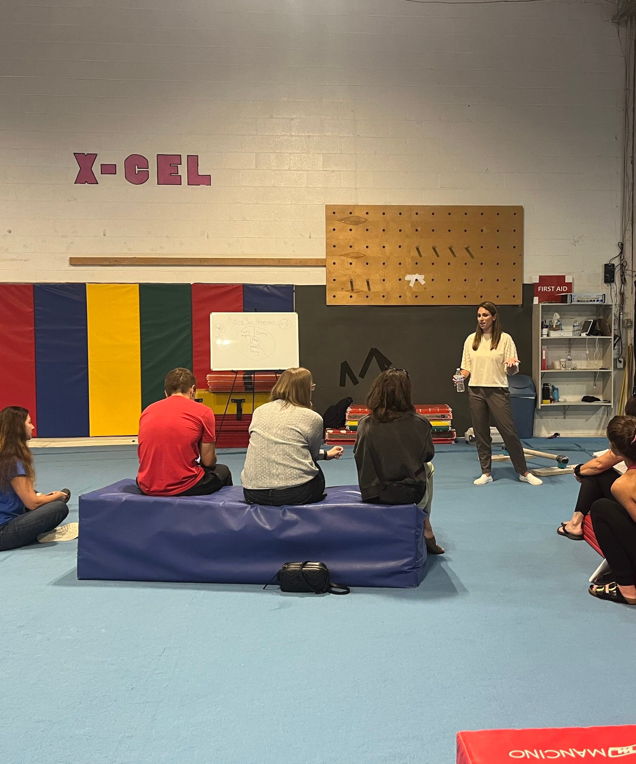 A group of gymnasts and parents seated together in a gym, attending a nutrition education workshop