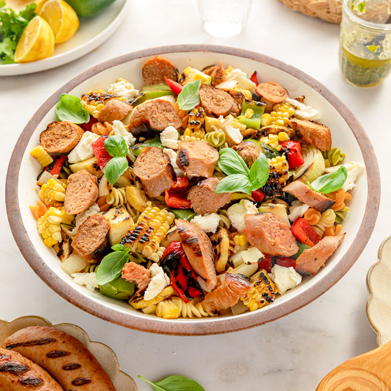 Grilled corn pasta salad featuring turkey sausage, cherry tomatoes, and mozzarella balls.
