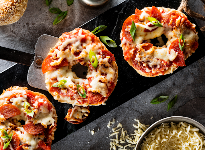 Write descriptive alt text for this image: A freshly prepared pizza bagel topped with melted mozzarella cheese, lean deli meat, and a sprinkle of Italian seasoning, served open-faced on a plate.