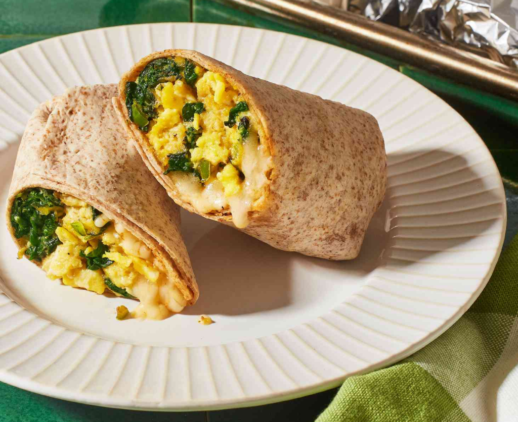 A freshly made egg and cheese breakfast burrito with spinach, avocado, and salsa on a plate, representing a nutritious post-practice recovery meal for gymnasts.