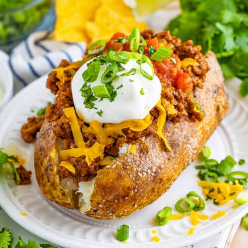 Write alt text for an image of a loaded baked potato topped with seasoned ground meat, melted shredded cheese, a dollop of Greek yogurt, and fresh green onions.