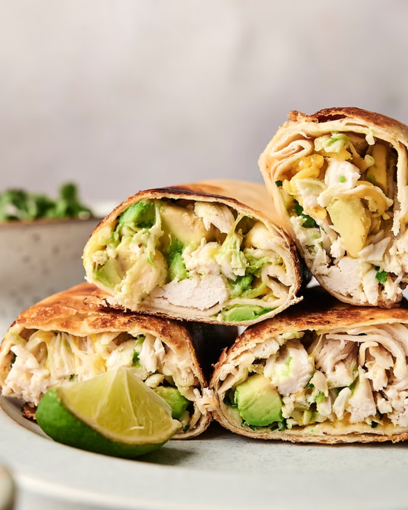 a whole grain wrap filled with avocado, chicken, and green vegetables
