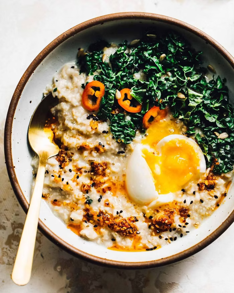 a savory oatmeal bowl with a runny egg, spinach, shredded melted cheese, and everything bagel seasoning
